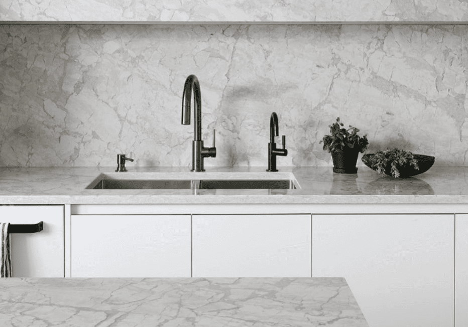 Modern kitchen with Pompeii Quartz Bahia/ Vicostone Quartz Bahia countertops and backsplash, dual black faucets, and white cabinetry.