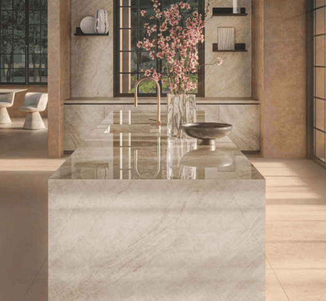 Luxurious kitchen with a porcelain waterfall island, made with Infinity Porcelain, Taj Mahal, gold faucet, and decorative vase with pink flowers.