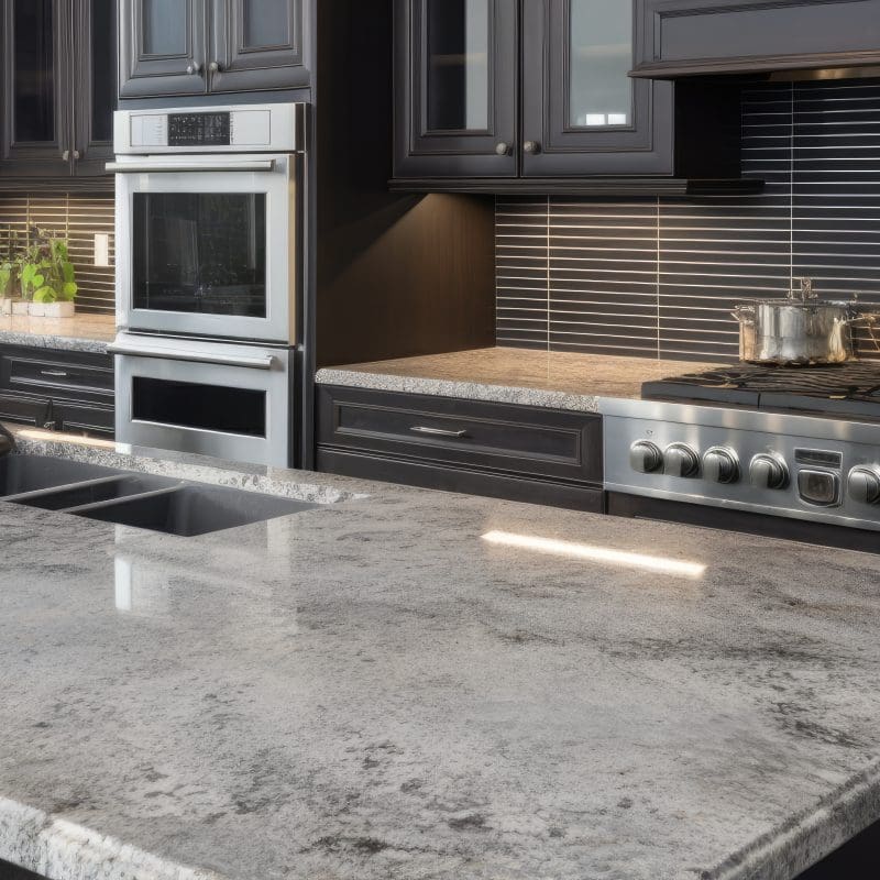 A modern kitchen with dark cabinets and light toned granite countertops.