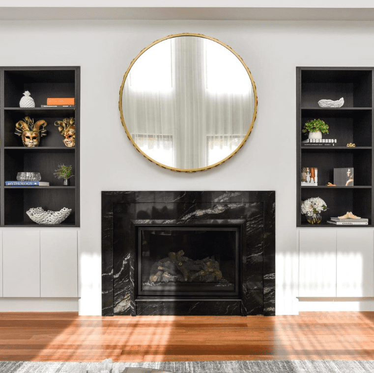 Black granite fireplace surround with built-in shelving and round mirror above.