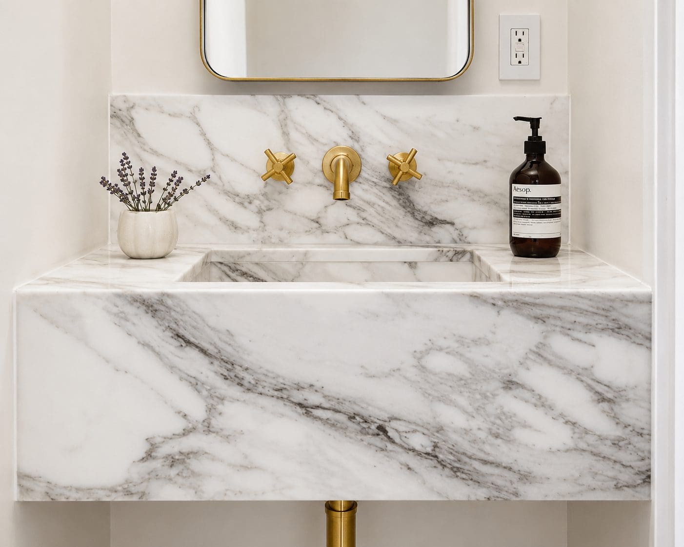Floating bathroom vanity with white marble featuring elegant gray veining and brass fixtures. 
