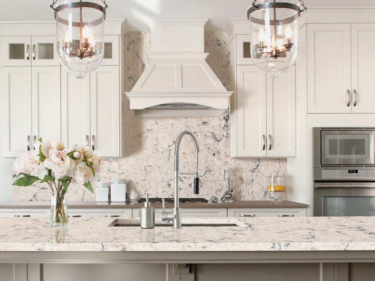 White kitchen with granite countertops and matching backsplash, lantern pendant lights, and a range hood.