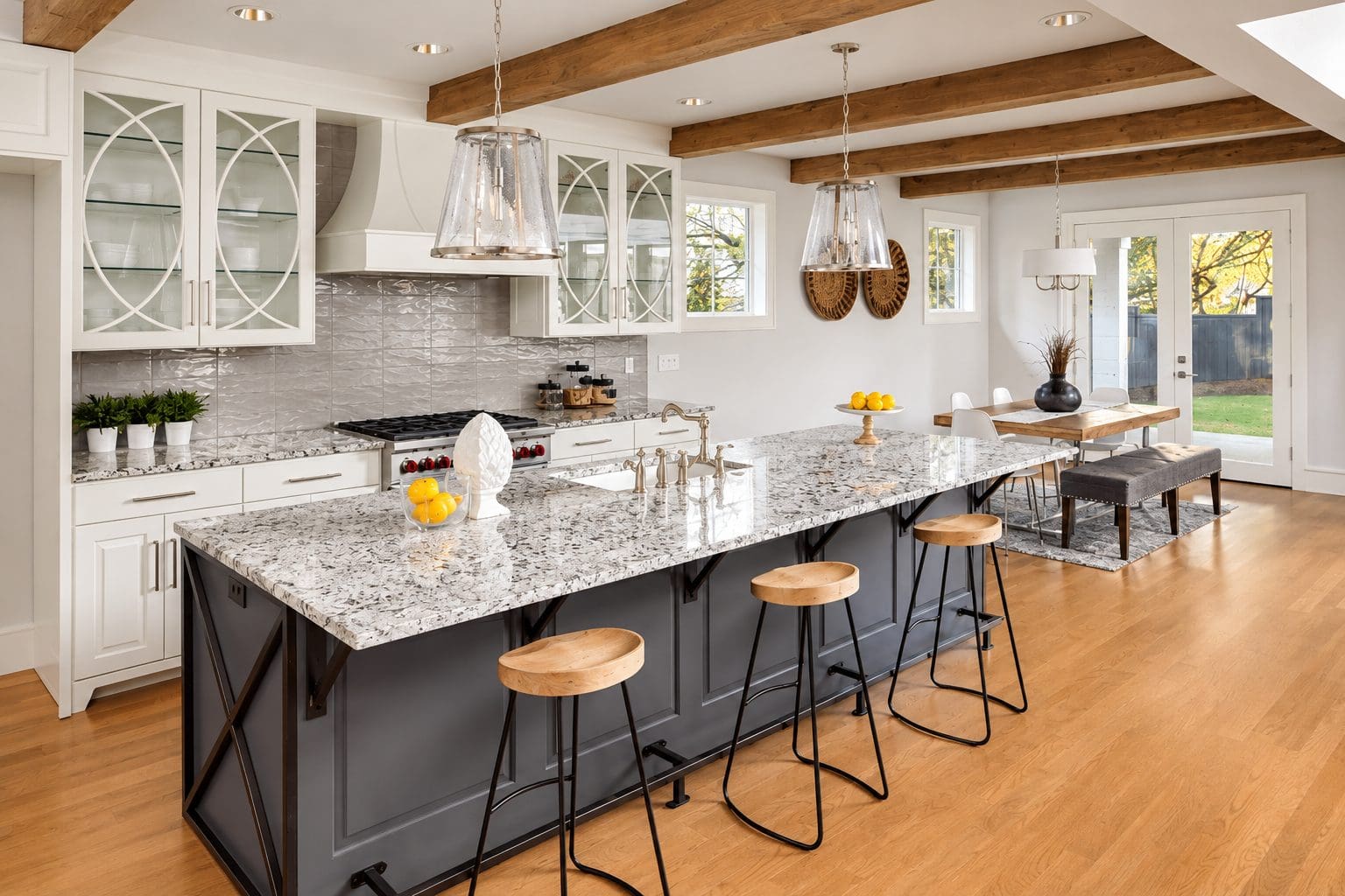 Farmhouse kitchen with granite island countertop, wood beam ceiling, and stools with metal legs. 